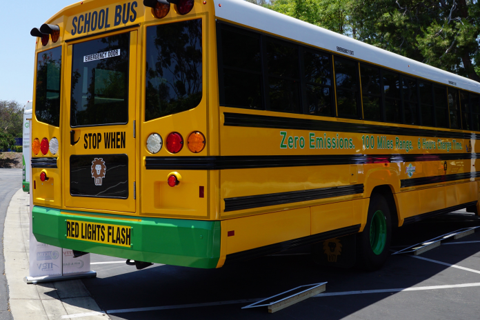 Photo of the rear of an electric school bus. Side of bus reads "Zero Emissions. 100 Miles Range."
