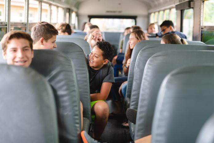 A photo of students sitting on the inside of a school bus. The students are laughing and talking to one another.