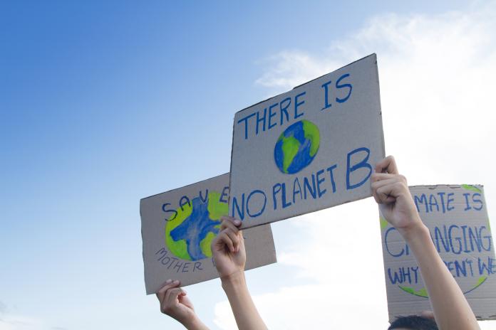 Hand-drawn signs being held in the air. Main sign reads, "There is No Planet B." 