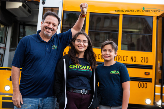 Three people stand in front of an electric school bus smiling as one raises his fist.