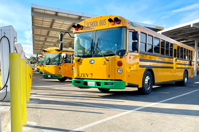 An electric school bus charges in a parking lot.