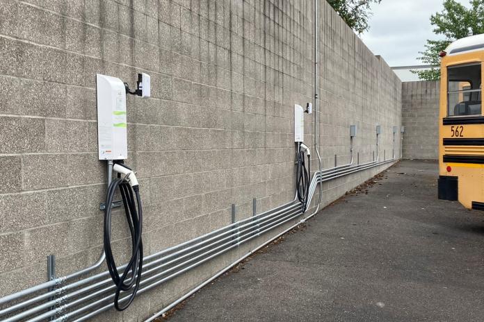 Electric school bus chargers and access points mounted to a brick wall, near the back of an electric school bus.