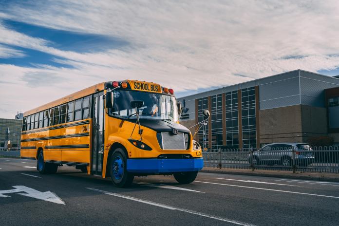 An electric school bus drives near a school.