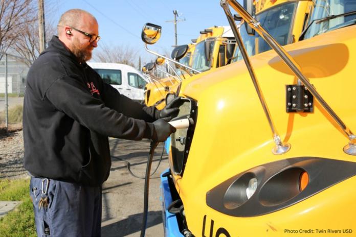 A person in a black sweatshirt charges an electric school bus.