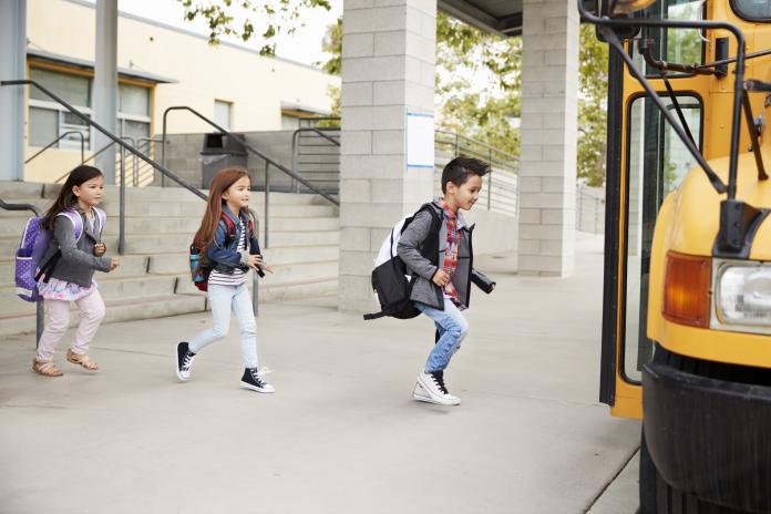 Young students in backpacks run to get on a school bus.