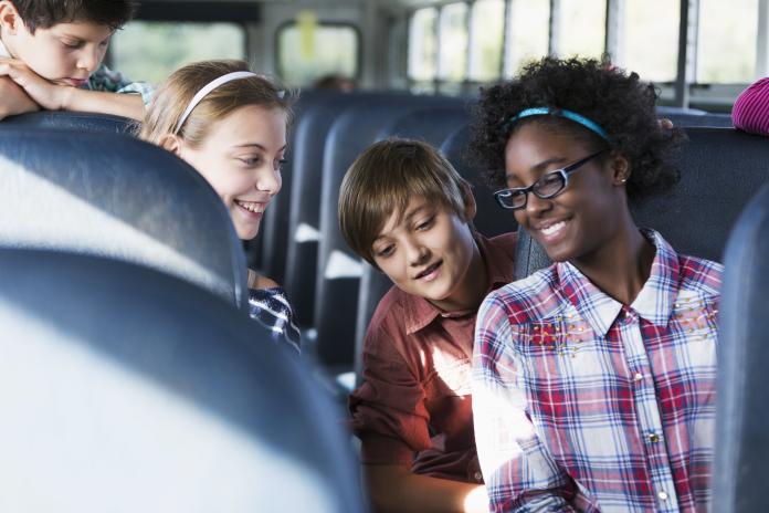 Students smile as they ride on a school bus. 