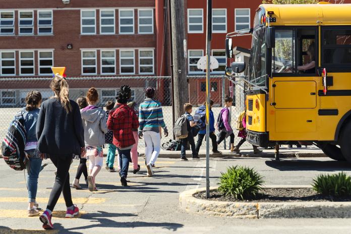 Students walk to a yellow school bus.