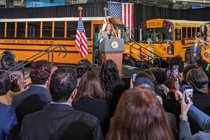 Vice President Kamala Harris speaks at a lectern in front of two electric school buses.
