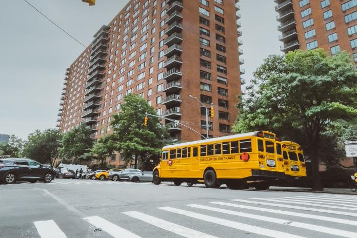 A school bus parked in a city next to a multi-story residential building.