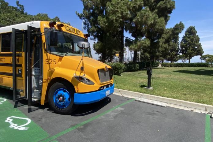 An electric school bus charges in a parking lot.