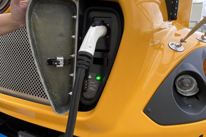 An electric school bus plugged in to its charger