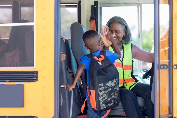 A bus driver high-fives a student boarding a school bus.