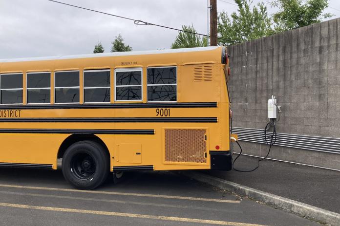 An electric school bus charges in a parking lot.