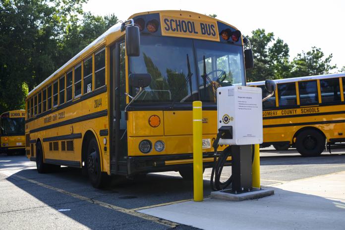 An electric school bus parked at a charging station in a lot.
