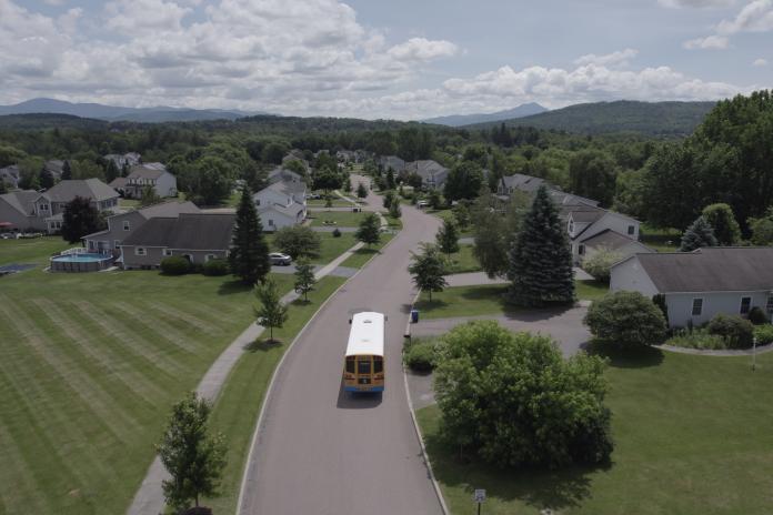 An electric school bus drives down a suburban street