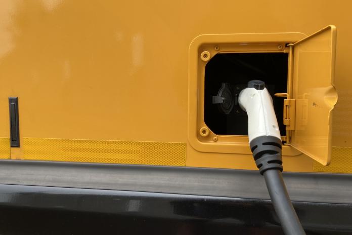 An electric school bus charger plugged into a port.