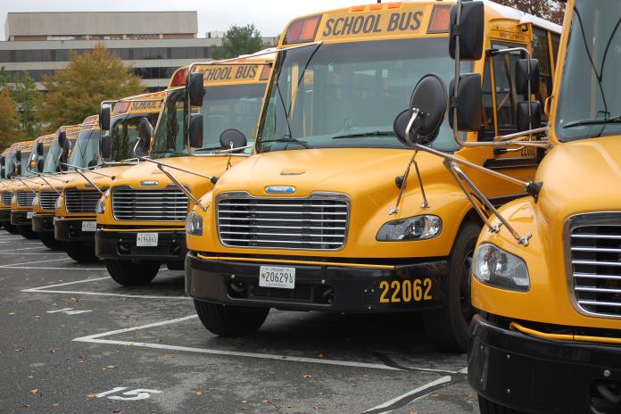 Front view of several electric school buses lined up in a bus depot.
