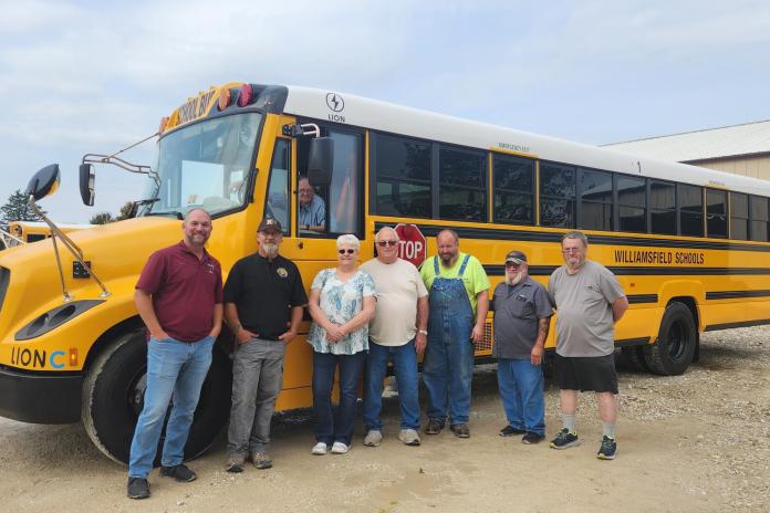 A group of people stand in front an electric school bus in Williamsfield, Illinois