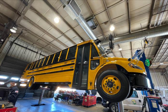 Electric school bus on a lift at a school district bus depot. 