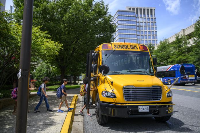 Students board an electric school bus parked on the street.