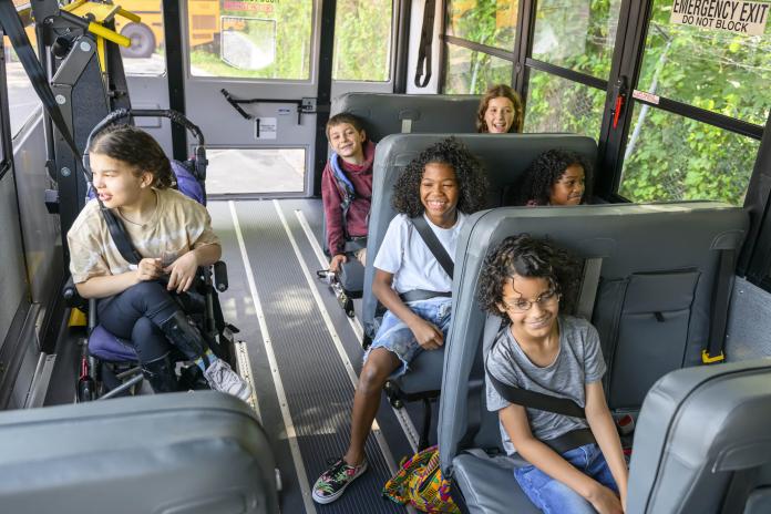 Diverse group of students, with and without disability, riding an accessible school bus.