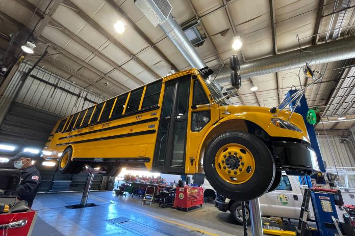 An electric school bus is elevated in a garage for maintenance.