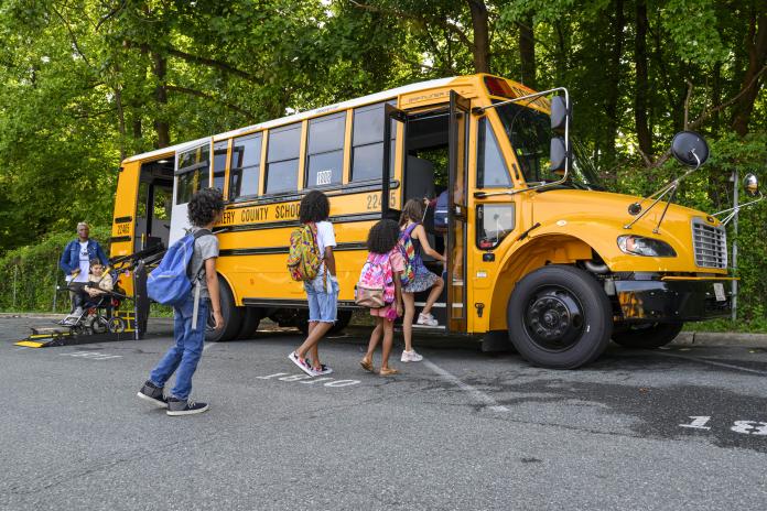 Kids board an electric school bus, including one student using a wheelchair lift