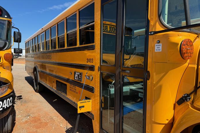An electric school bus charges while parked under the sun