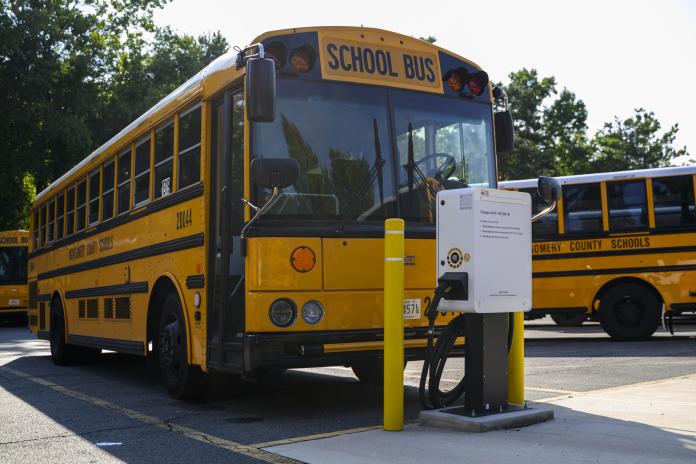 Electric school bus charging in parking lot.