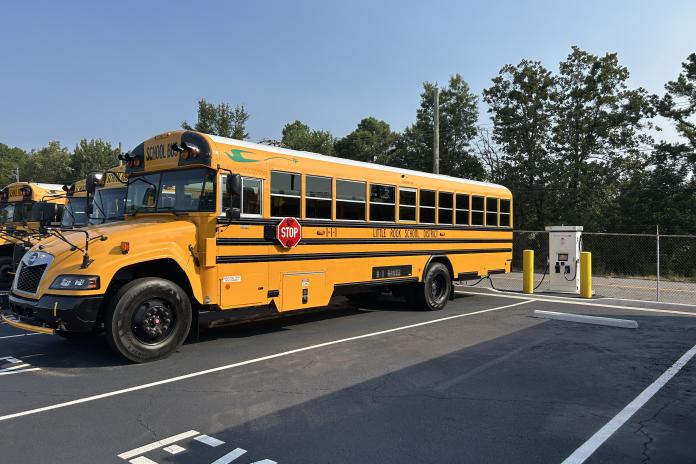An electric school bus charges in a parking lot