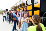 An elementary age girl with Down Syndrome gives a fist bump to a female school bus driver. The girl and other students are boarding the school bus.