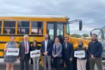 Electric school bus advocates and lawmakers stand in front of a school bus, holding signs that read "Electric Buses 4 Texas"