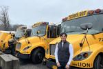 A person stands in front of a row of parked electric school buses.