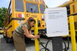 A worker plugs an electric school bus in to a charger.