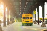 A yellow school bus drives down a road underneath a bridge.