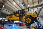 An electric school bus is elevated in a garage for maintenance.