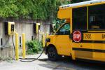 A yellow electric school bus is parked and plugged in to a charger.