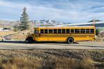 A yellow electric school bus outside on the road in front of mountains.