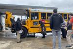 A group of people stand in front of an electric school bus with its hood open