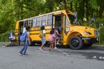 Kids board an electric school bus, including one student using a wheelchair lift