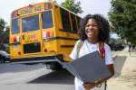 A student holds a folder near an electric school bus and smiles.