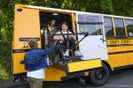 A student uses a wheelchair lift to deboard a school bus with the help of two adults.