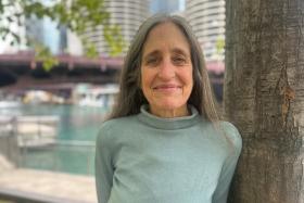 Susan Mudd smiles while standing near a tree and a river.