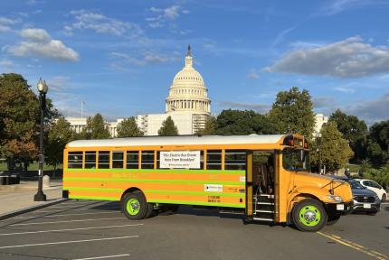 An electric school bus in a parking lot near the US Capitol building.
