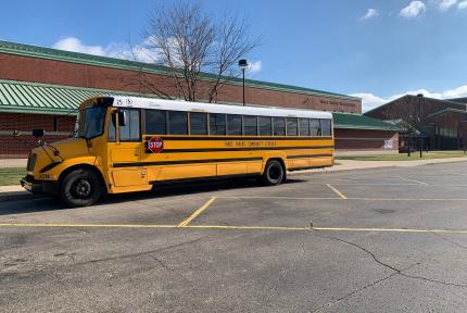 A yellow school bus is parked outside of a school under a blue sky. The school sign reads "Three Rivers High School."