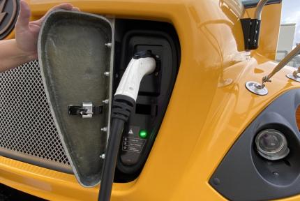 An electric school bus plugged in to its charger