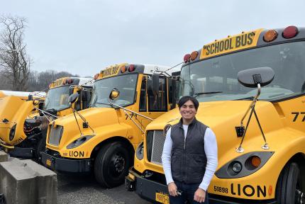 A person stands in front of a row of parked electric school buses.