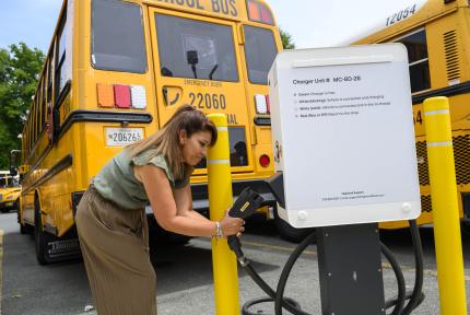 A worker plugs an electric school bus in to a charger.