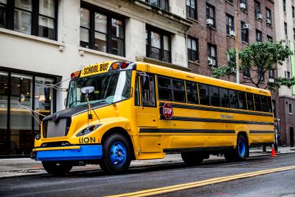 An electric school bus drives on a city road.
