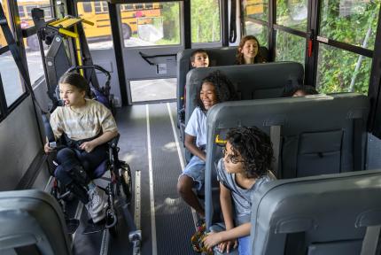 A group of students smile and talk on a school bus.